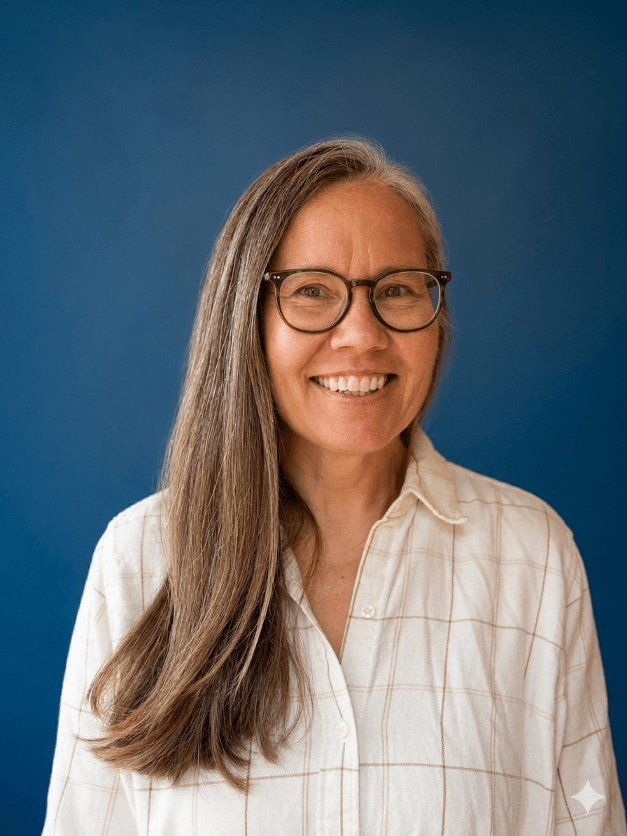 Smiling woman with long grey hair and glasses in a white plaid shirt against blue.