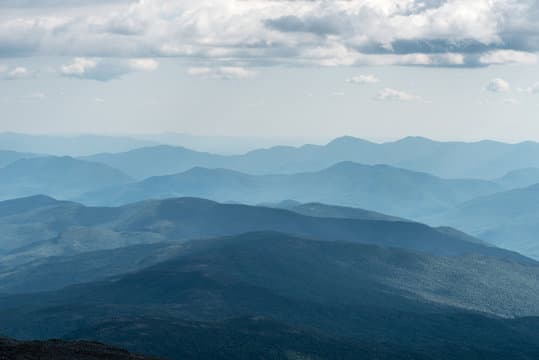 Rolling blue mountain ridges layer into the distance under a soft, cloudy sky.